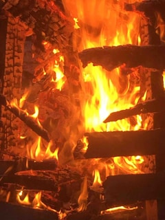 Bright flames engulf stacked logs, creating an intense and dynamic display of fire with vivid, swirling patterns.