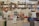 A bookstore with shelves filled with a variety of books arranged neatly. There is a table in the foreground stacked with several different books with colorful covers, featuring notable authors and titles. Books are stacked both vertically and horizontally, showcasing different genres.