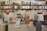 A bookstore with shelves filled with a variety of books arranged neatly. There is a table in the foreground stacked with several different books with colorful covers, featuring notable authors and titles. Books are stacked both vertically and horizontally, showcasing different genres.