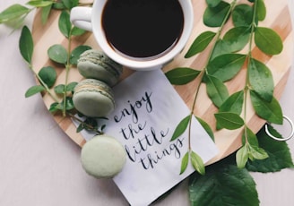 flat lay photography of leaves with cup of coffee and three macarons on chopping board