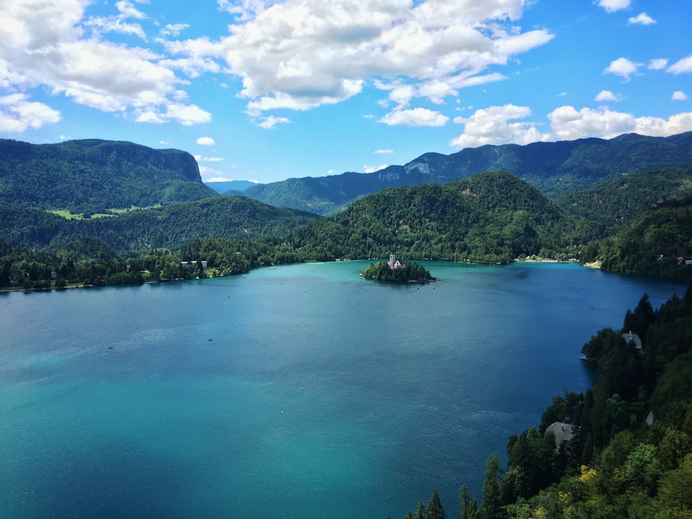 turquoise and azur body of water surrounded by mountain range and forest under white clouds and blue sky at daytime