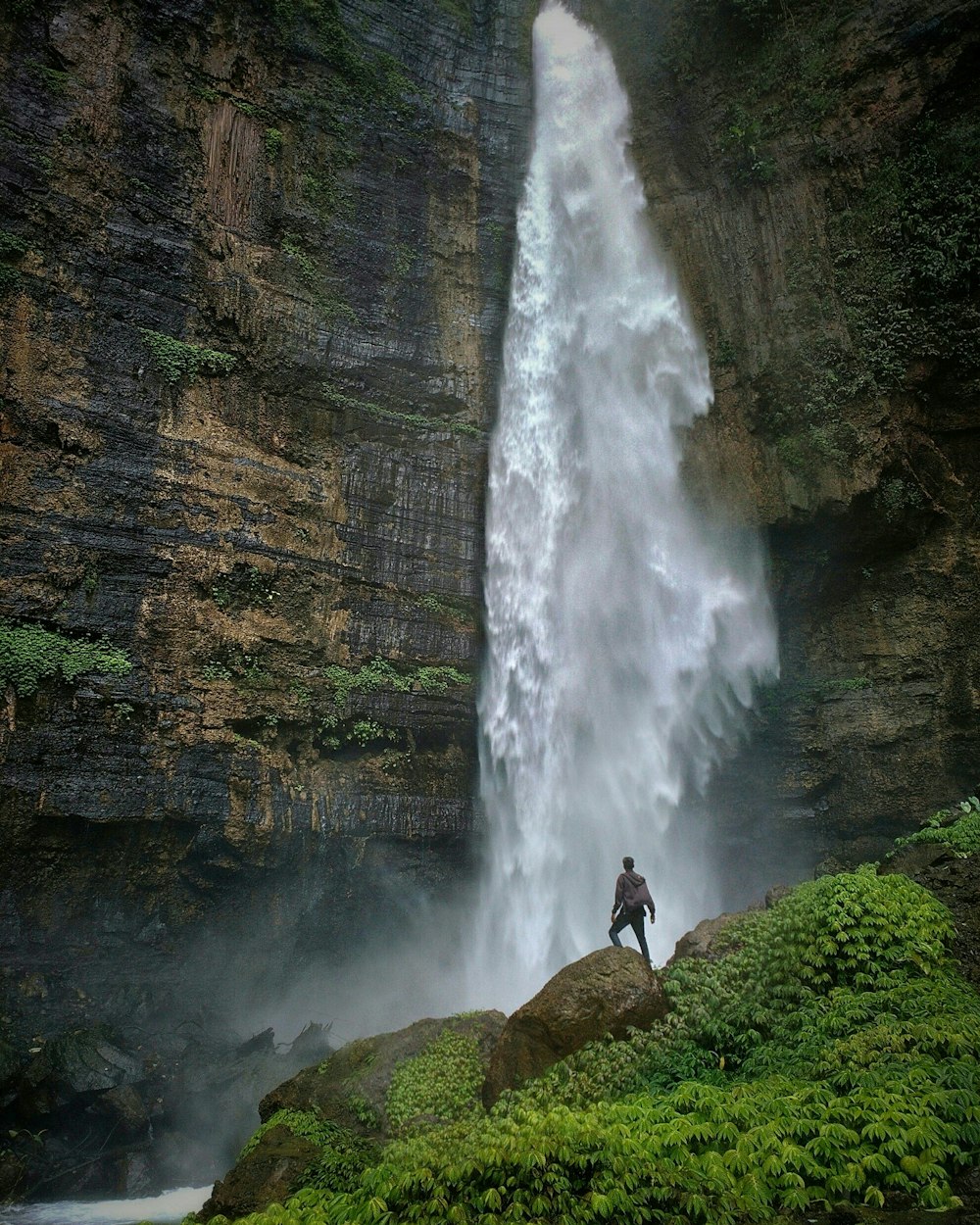 昼間、茶色の岩層に立って滝を眺める人
