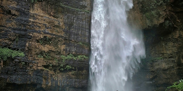 person standing on brown rock formation looking at waterfalls during daytime