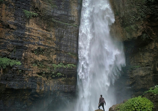 person standing on brown rock formation looking at waterfalls during daytime