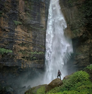 person standing on brown rock formation looking at waterfalls during daytime