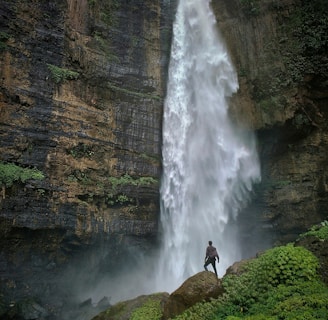 person standing on brown rock formation looking at waterfalls during daytime