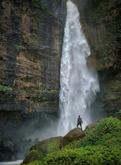 person standing on brown rock formation looking at waterfalls during daytime