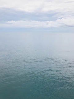 A calm ocean horizon with soft clouds reflecting on the water’s surface.