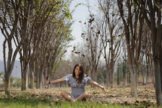 A joyful woman standing in a sunlit forest, arms open wide embracing nature's calm.