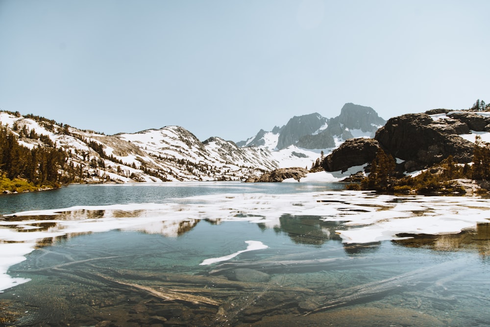 Montaña verde cubierta de nieve cerca del cuerpo de agua durante el día