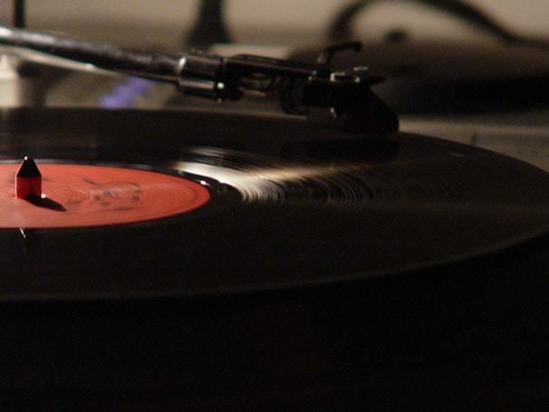 A close-up view of a spinning vinyl record on a turntable, with a distinct red label in the center and a stylus gently gliding over the grooves. Lighting highlights the texture of the vinyl, creating a warm and nostalgic ambiance.