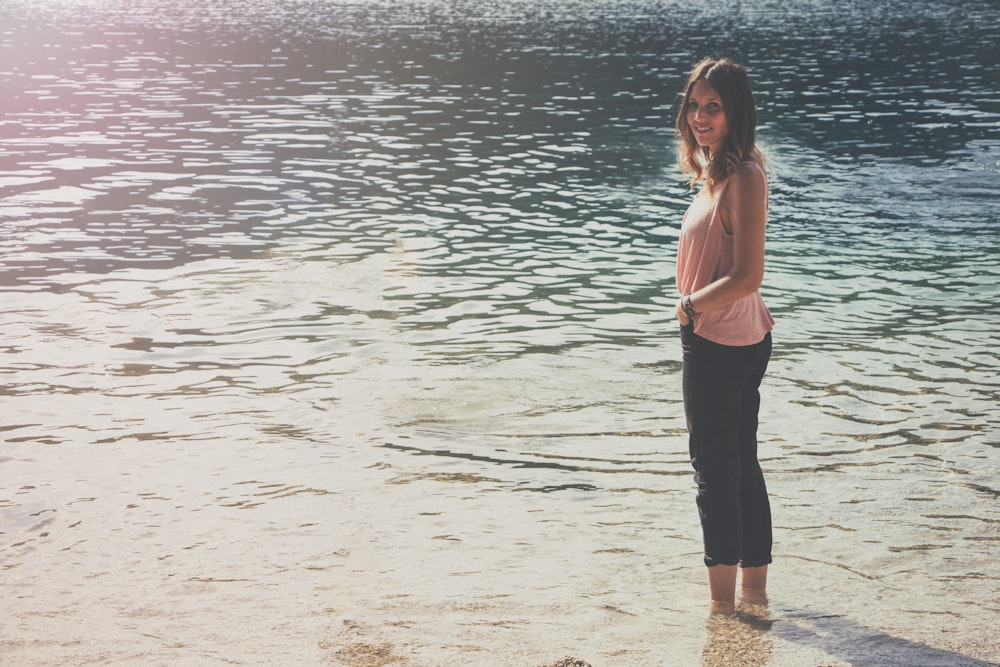 Femme en haut rose sans manches et pantalon cargo noir debout sur un plan d’eau