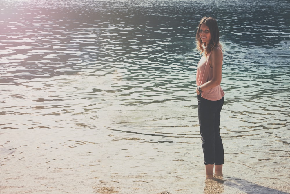 woman in pink sleeveless top and black cargo pants standing on body of water