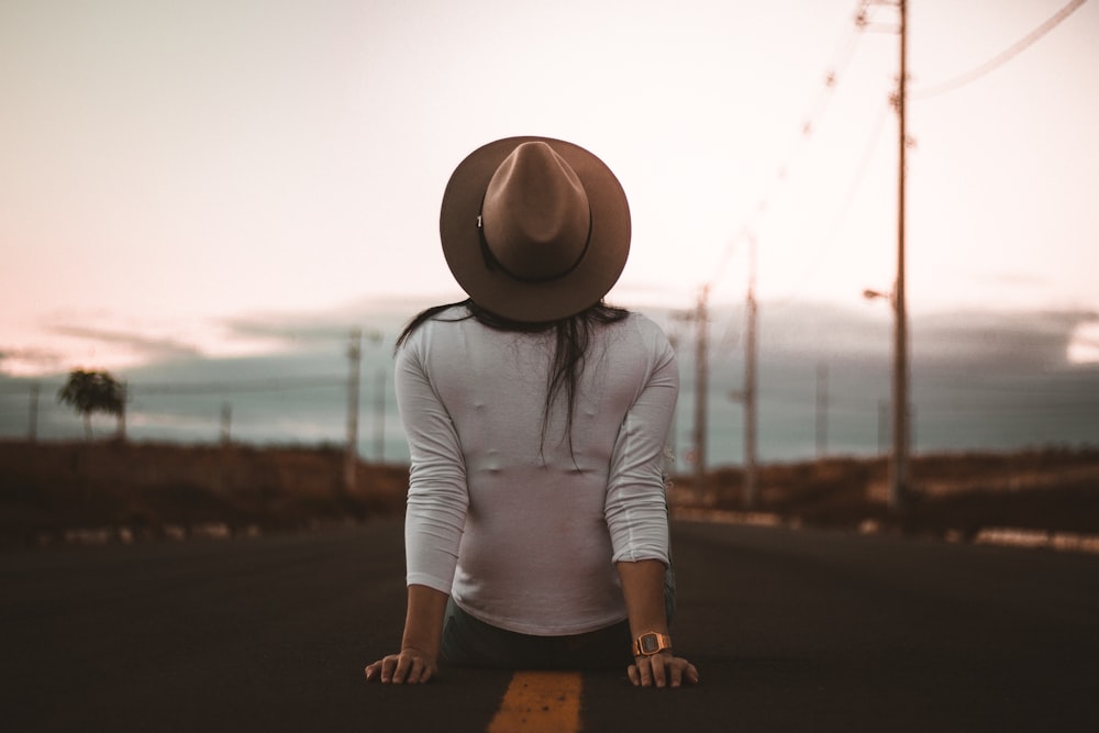 woman sitting on road wearing white shirt and brown hat