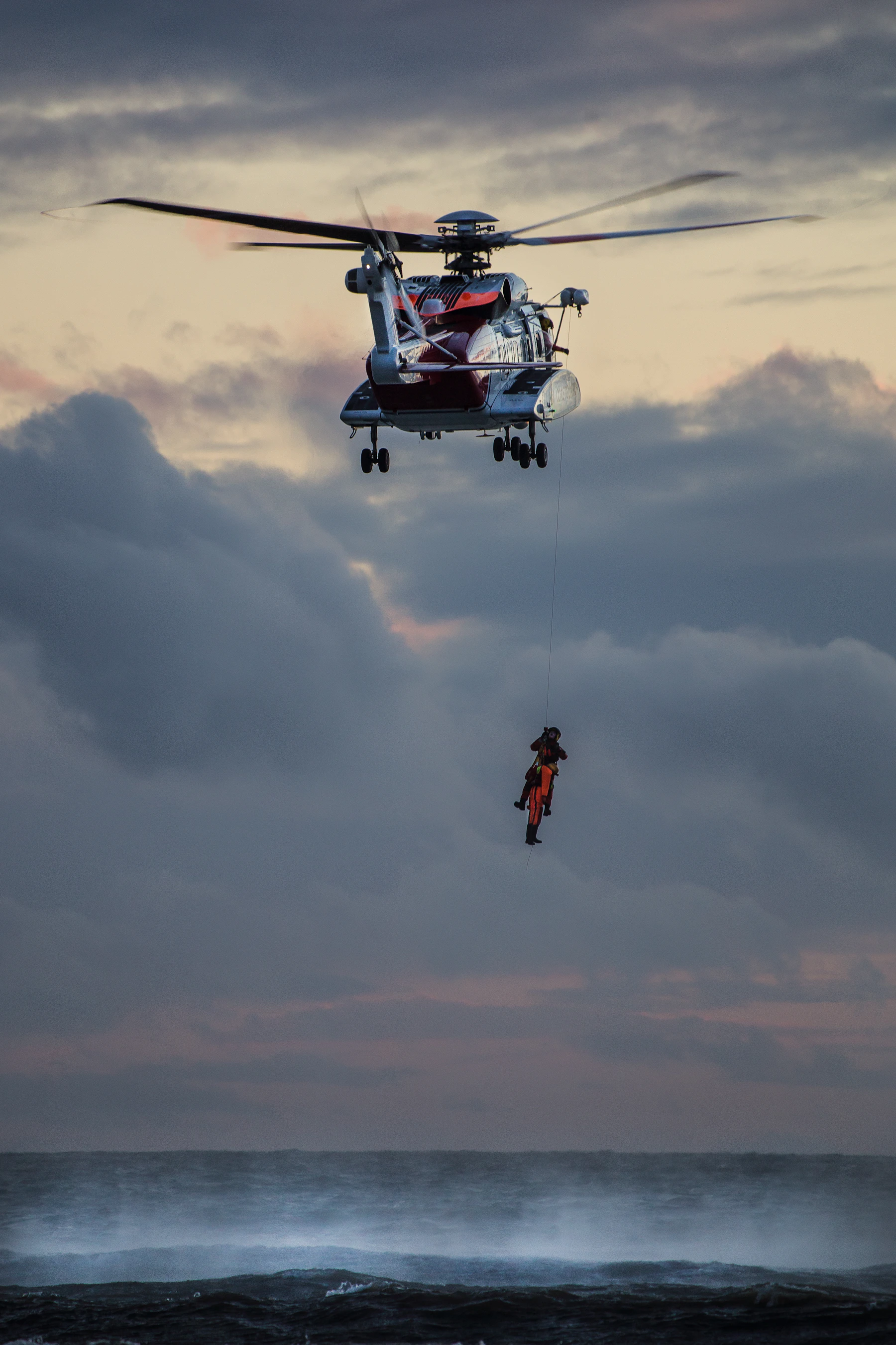 Helicopter hoisting a person from open water during an active search and rescue operation
