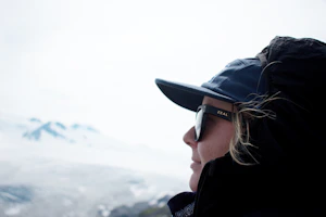 Outdoor explorer wearing wrap-around polarized sunglasses and a Flexcore technical cap against a snowy peak backdrop