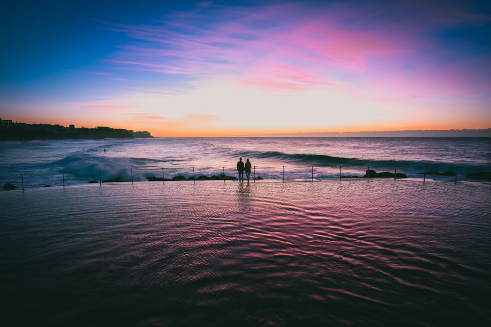 Couple holding hands at sunset on the edge of infinity pool by the ocean at Bronte Beach