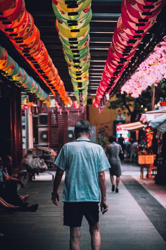 man in collared shirt walks between building during daytime in Chinatown Singapore Singapore