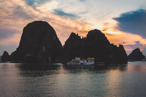 Sunset over limestone cliffs in Thailand's Halong Bay, boats gently floating on calm waters.