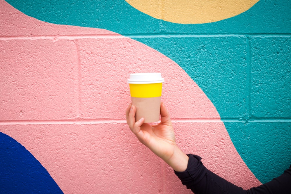 Person holding a plastic coffee cup in front of colorful wall at Venice Beach