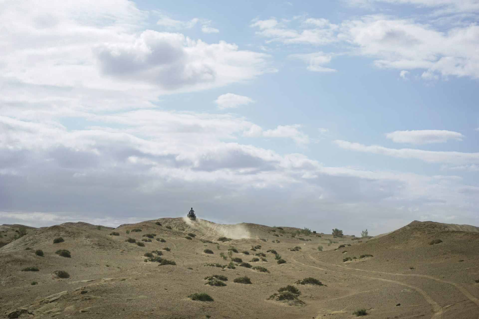 Close-up of a rider gripping the handlebars, dust swirling around, with the endless sandy landscape stretching out ahead.