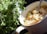 A dish of creamy chicken and vegetable stew is situated next to a fresh bunch of green leafy herbs in a white bowl with a spoon. The vegetables include sliced carrots and celery, adding vibrant colors to the dish.