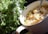A dish of creamy chicken and vegetable stew is situated next to a fresh bunch of green leafy herbs in a white bowl with a spoon. The vegetables include sliced carrots and celery, adding vibrant colors to the dish.