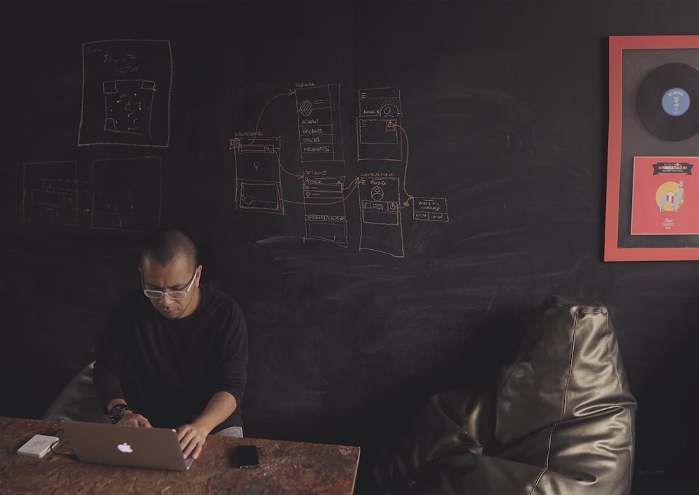 man sitting near table facing gray MacBook