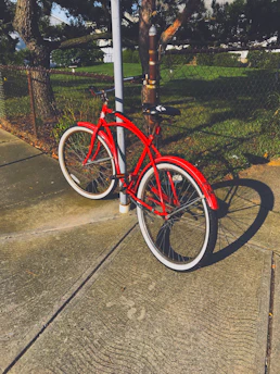 A bright red kids' bike resting on a sunny park path surrounded by colorful flowers.