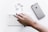 A hand is holding a pen over a weekly planner with sections for different days, placed on a white surface. Nearby, there is a silver iPhone and several metal paper clips.