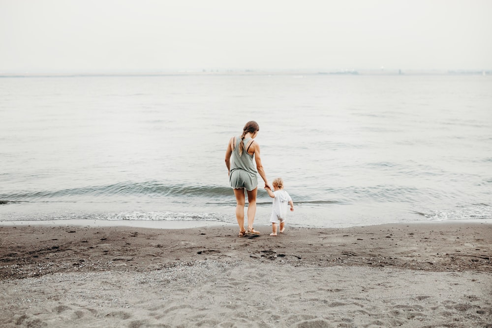 낮에 회색 모래 해변을 걷는 여자와 아기