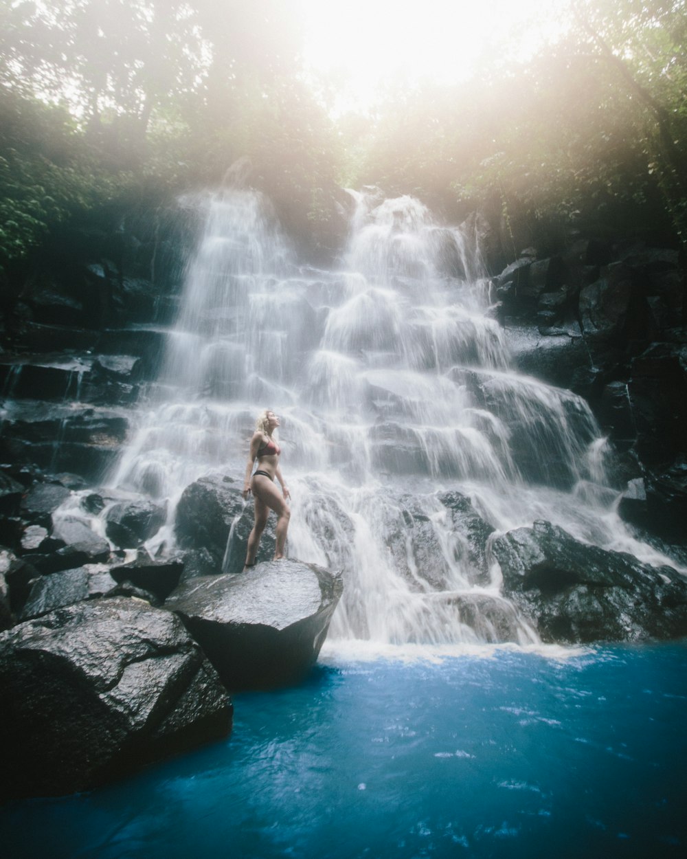 woman standing on rock monolith below waterfall