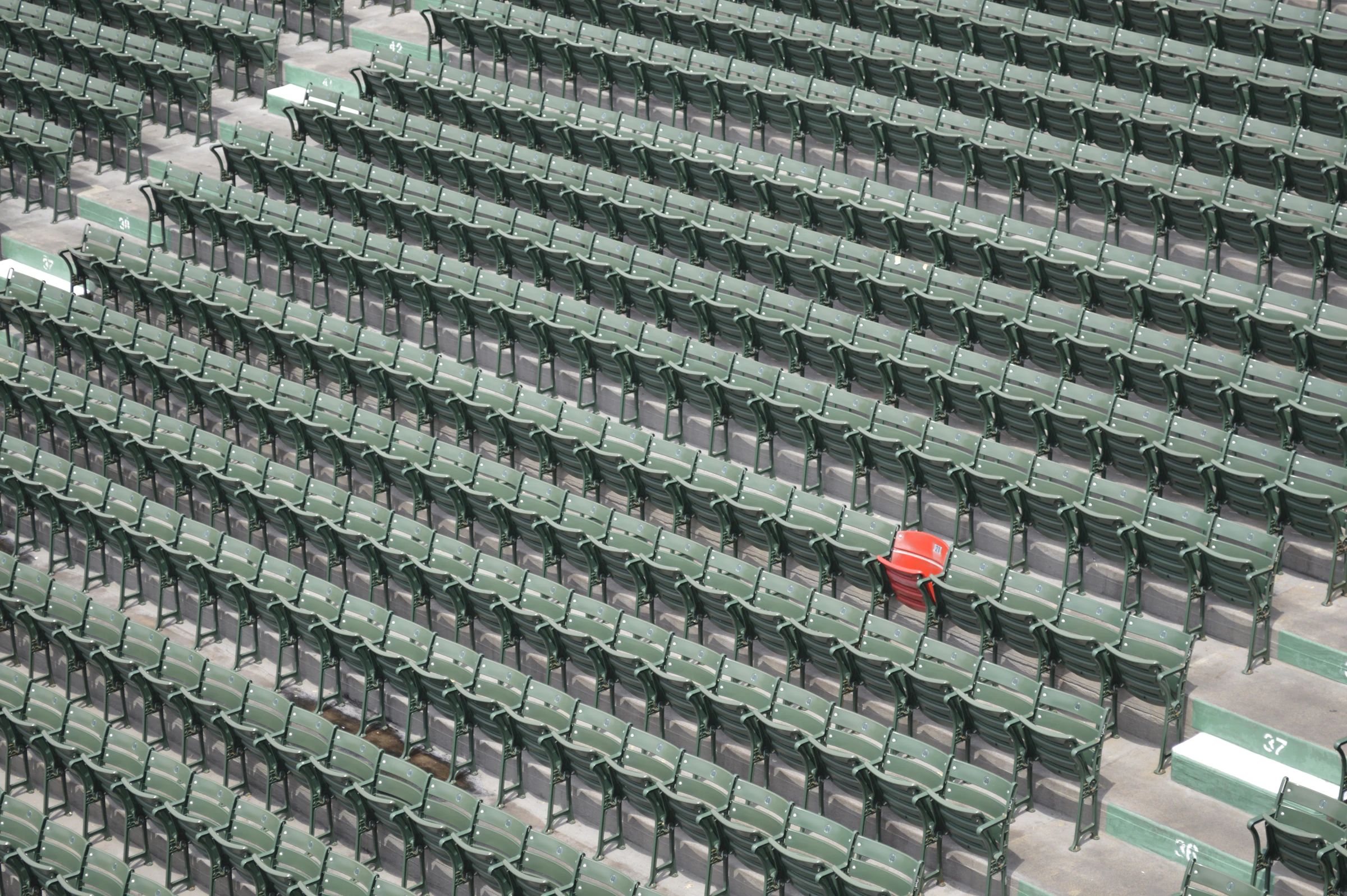 Row upon row of empty stadium seats climbing a grandstand, with a single red seat in the middle of the section.