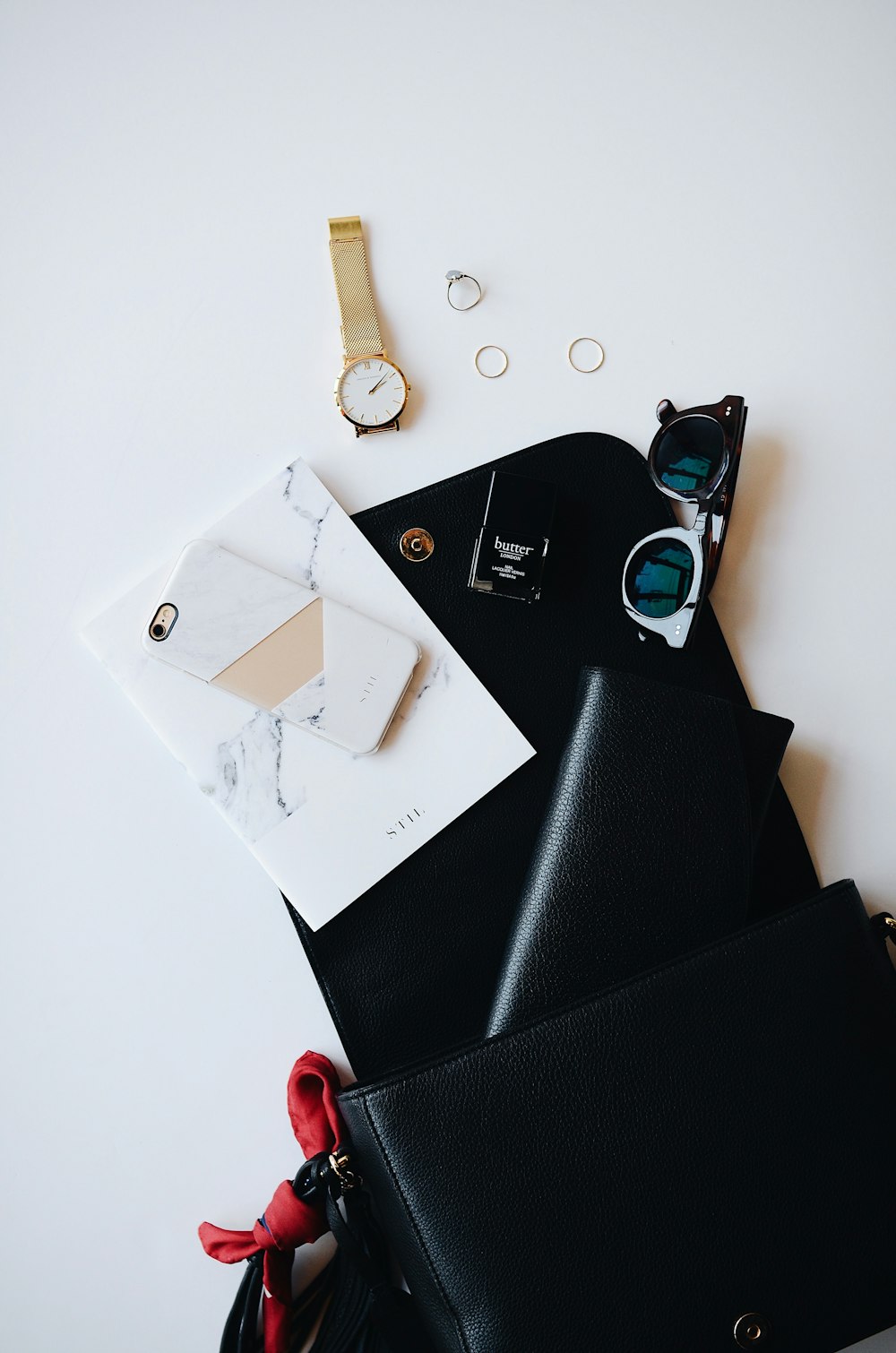 금색 시계, 흰색 스마트 폰, 가죽 지갑 및 안경과 같은 임의의 항목으로 덮인 검은 색 클립 보드.