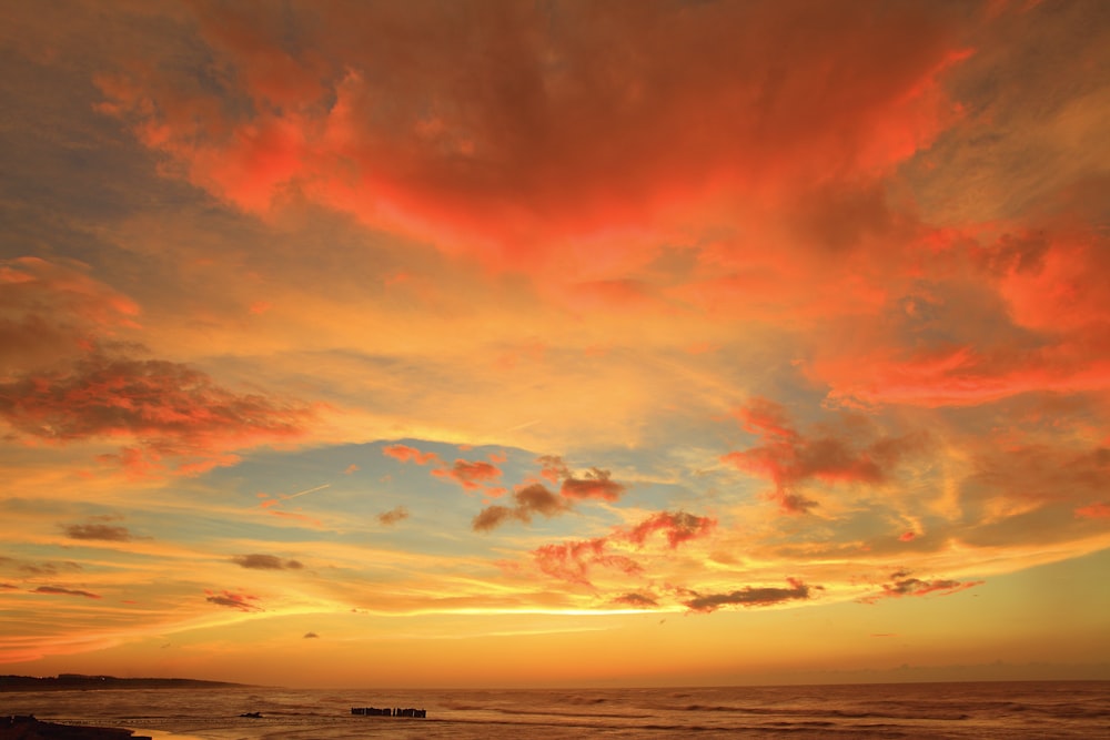 silhouette photo of body of water under orange clouds