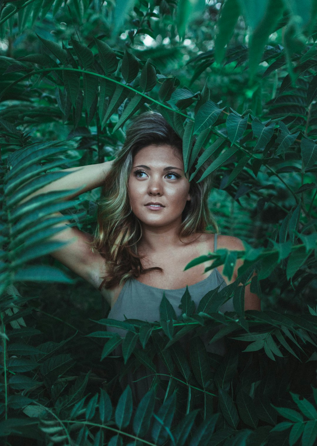 woman in green sleeveless dress surrounded with green leaves at daytime