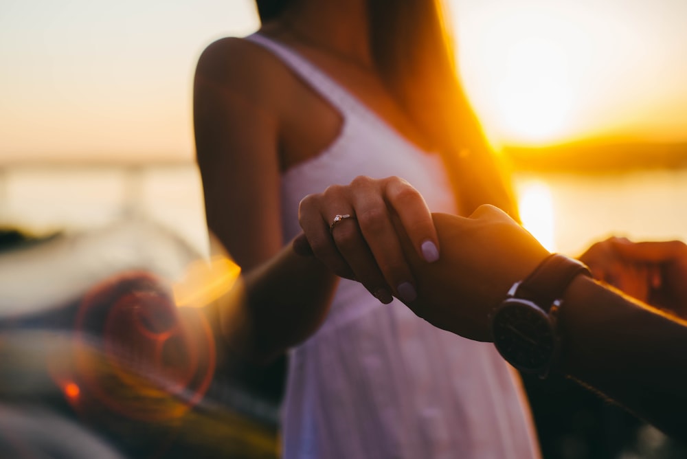 selective focus photography of woman wearing white sleeveless dress holding human hand during golden hour