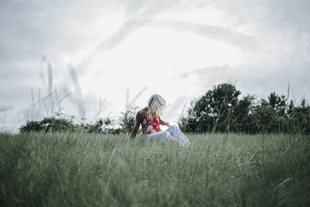 woman in red shirt and white pants sitting on green grass field