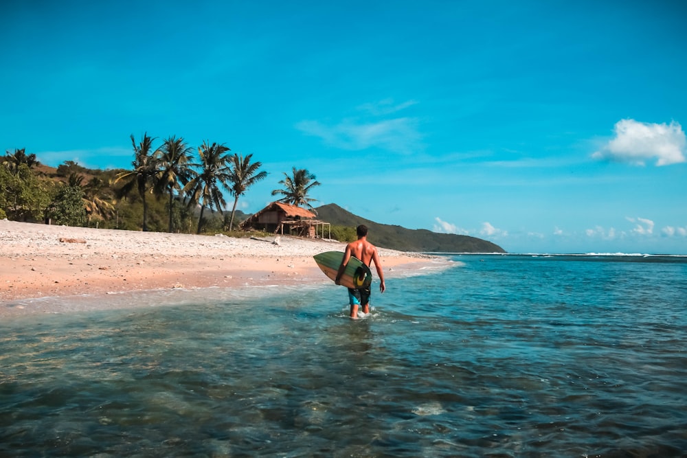 man holding surf board in body of water