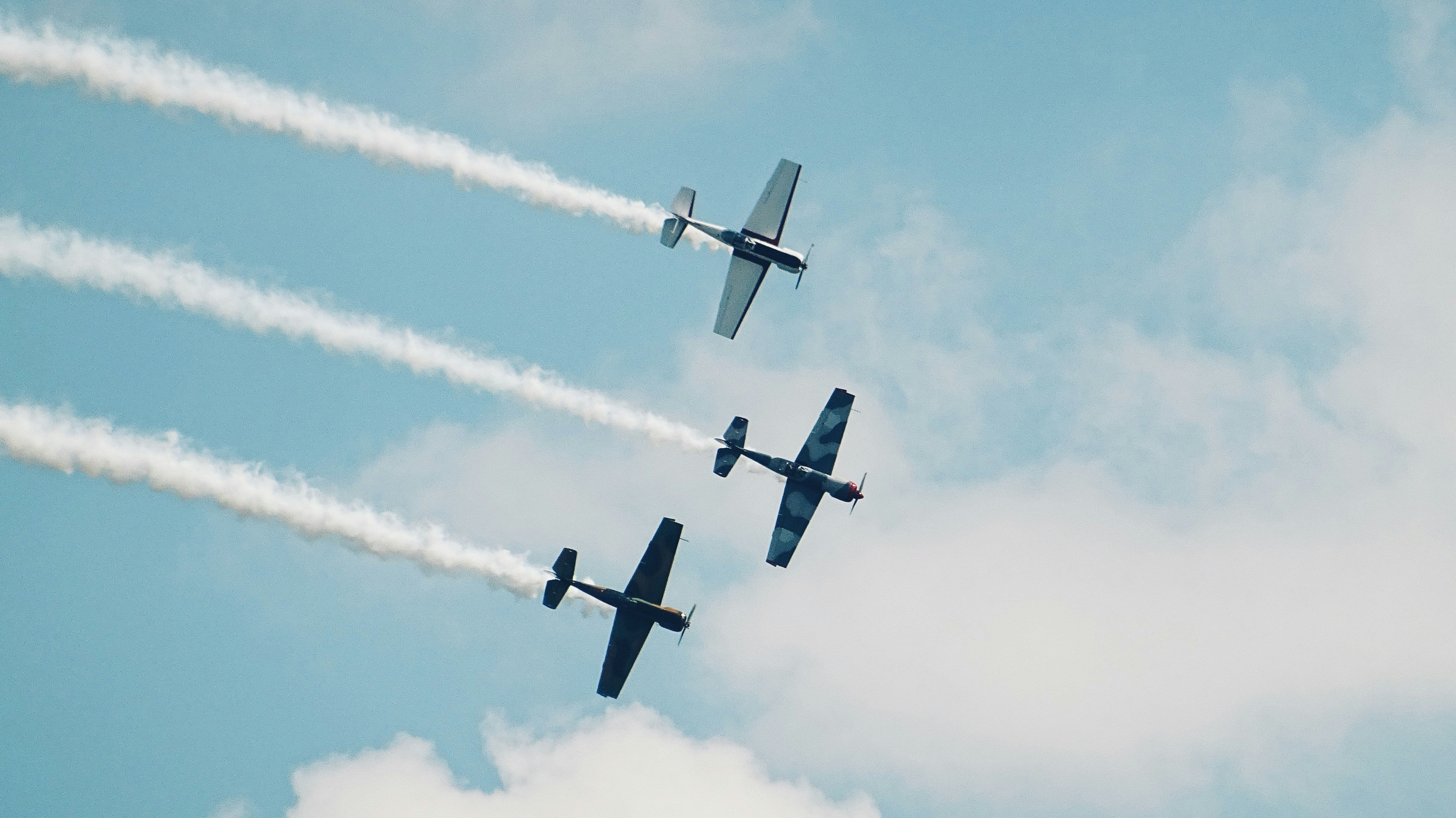 black, blue, and gray monoplanes in mid-air under white clouds, vintage plane formation