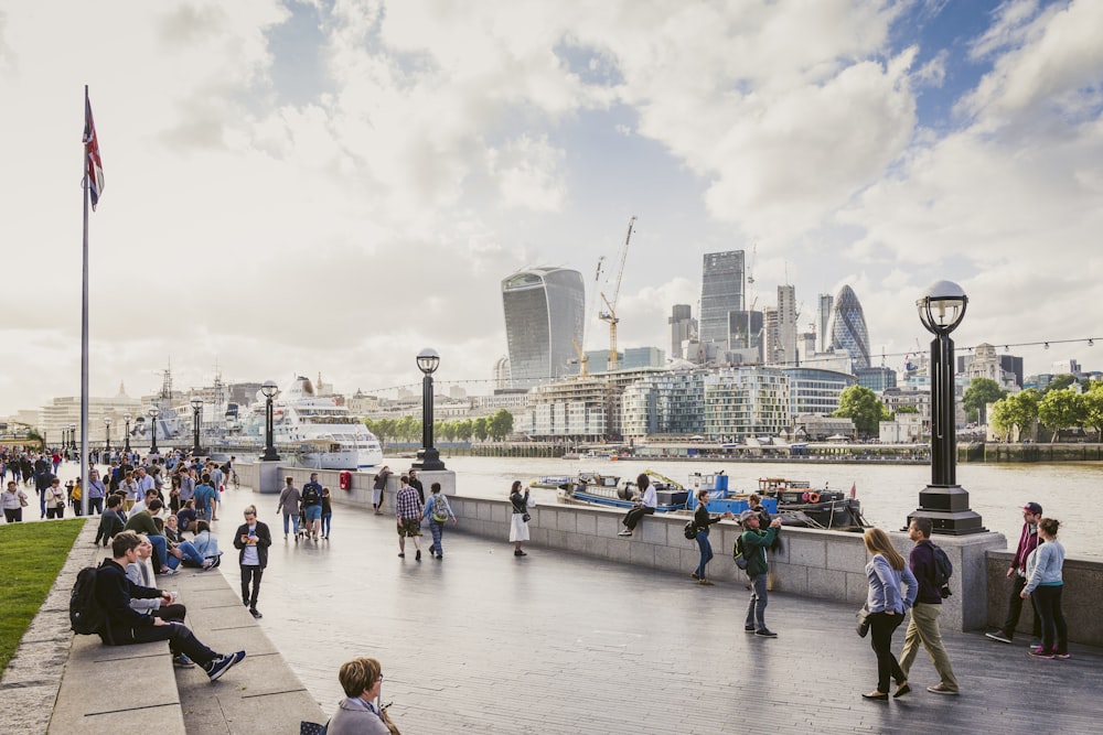 Turisti che passeggiano sulla riva del Tamigi con la City di Londra visibile sull'altra sponda