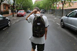 boy wearing white shirt and black shorts carrying backpack standing on black concrete road between vehicles and trees during daytime