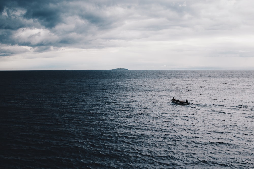 fotografia de baixa luz do barco na água do oceano sob céu nublado