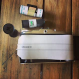 A handcrafted pinhole camera resting on a wooden table with film rolls nearby.