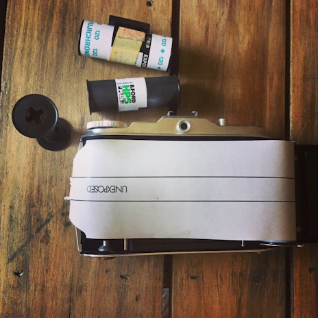 A vintage pinhole camera resting on a textured wooden table with film rolls nearby.