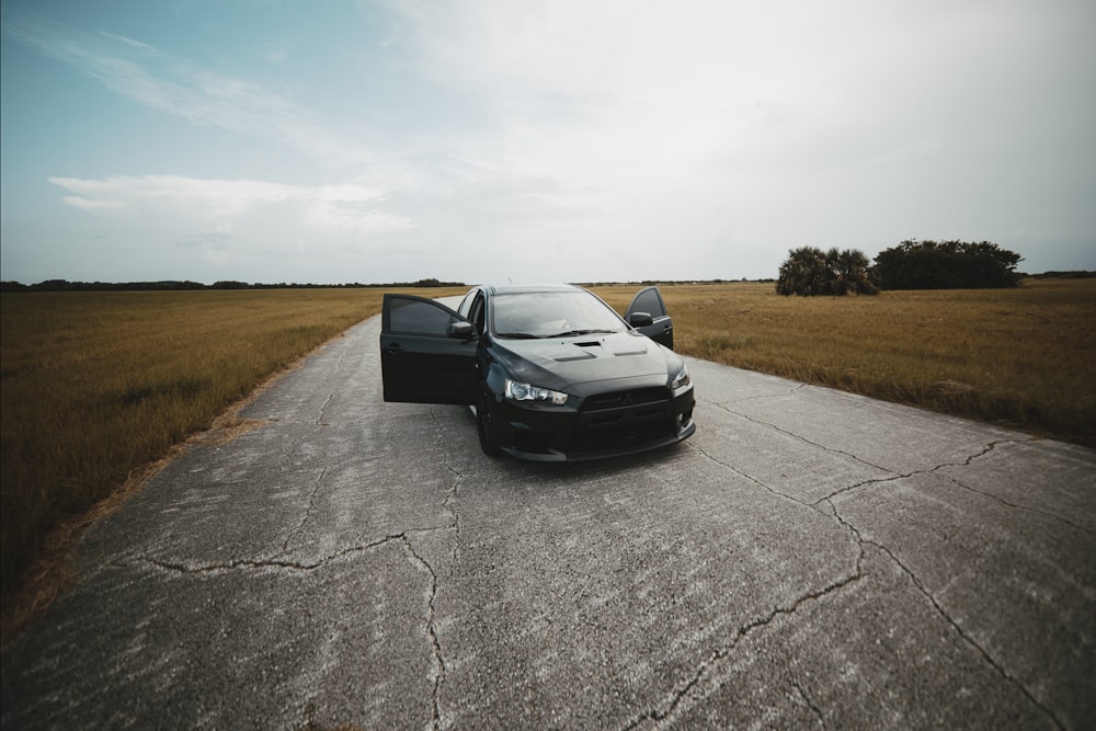 black vehicle with two opened doors parked on cracked gray road