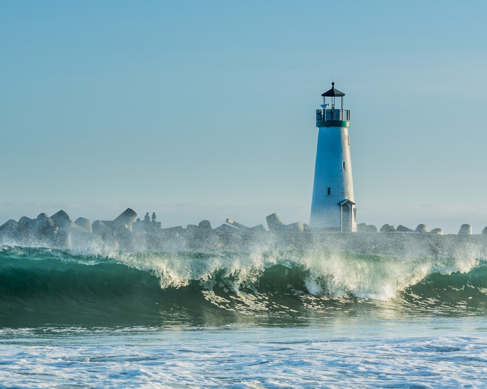 concrete lighthouse near rocks and ocean wave at daytime