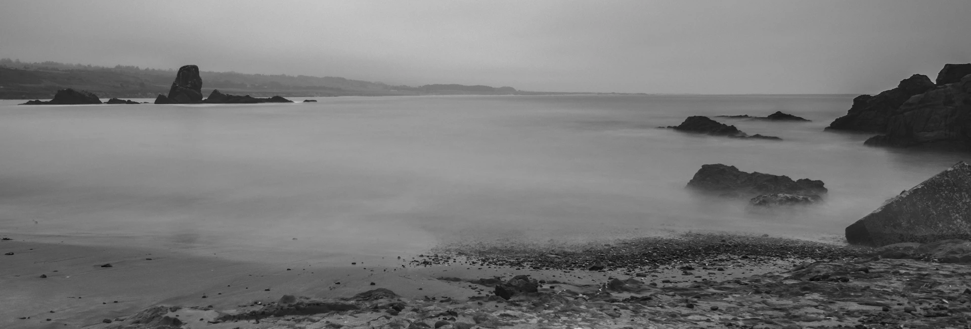 A serene black and white photo of a calm sea horizon with gentle waves under a cloudy sky.