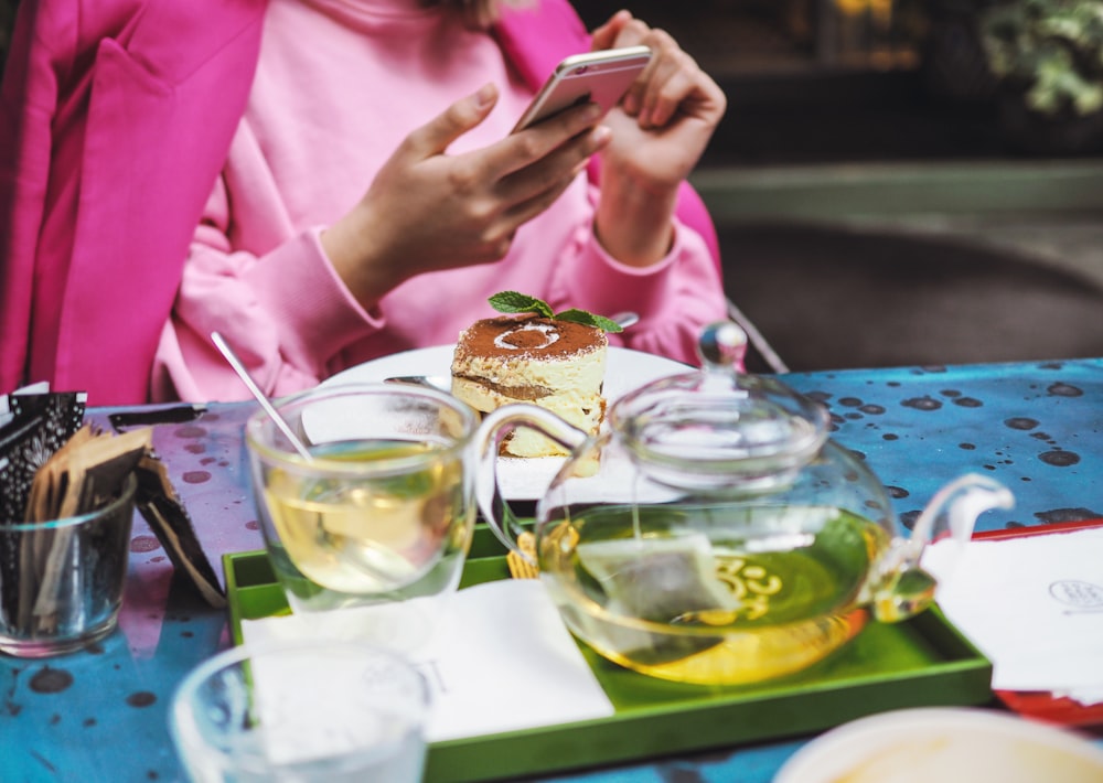 テーブルの横に座り、金色のiPhone 6を持ちながらお茶を飲む女性