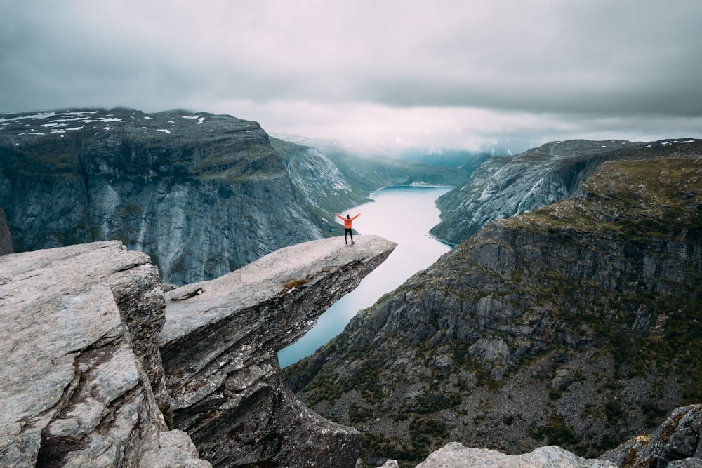 person standing on gray high-rise rock formation at daytime